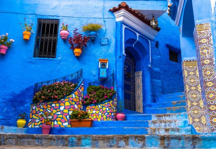 Blue steps and a mosaic planter outside a studded door in Chefchaouen